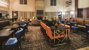 A spacious hotel lobby with a stone fireplace, multiple seating areas, and a large flat-screen TV mounted on the wall. - La Quinta Inn & Suites by Wyndham Ely (Ely)
