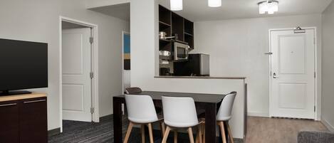 A modern kitchen with a microwave, stove, and cabinets, a dining area with a table and chairs, and a flat-screen TV on a cabinet.