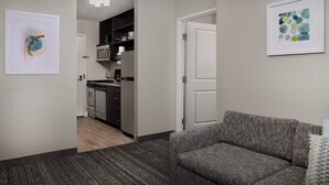 A modern living room with a grey sofa, a kitchen in the background, and artwork on the walls.