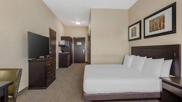 Une chambre d’hôtel avec un grand lit, une télévision, un bureau et une chaise. Une porte donne accès à une petite cuisine et à une salle de bain.