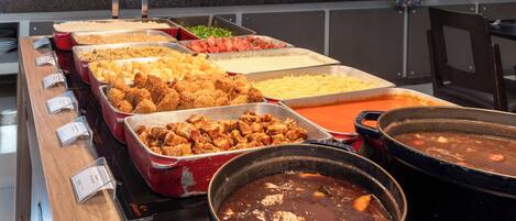 A buffet with various dishes including fried chicken, pasta, and a large pot of stew.