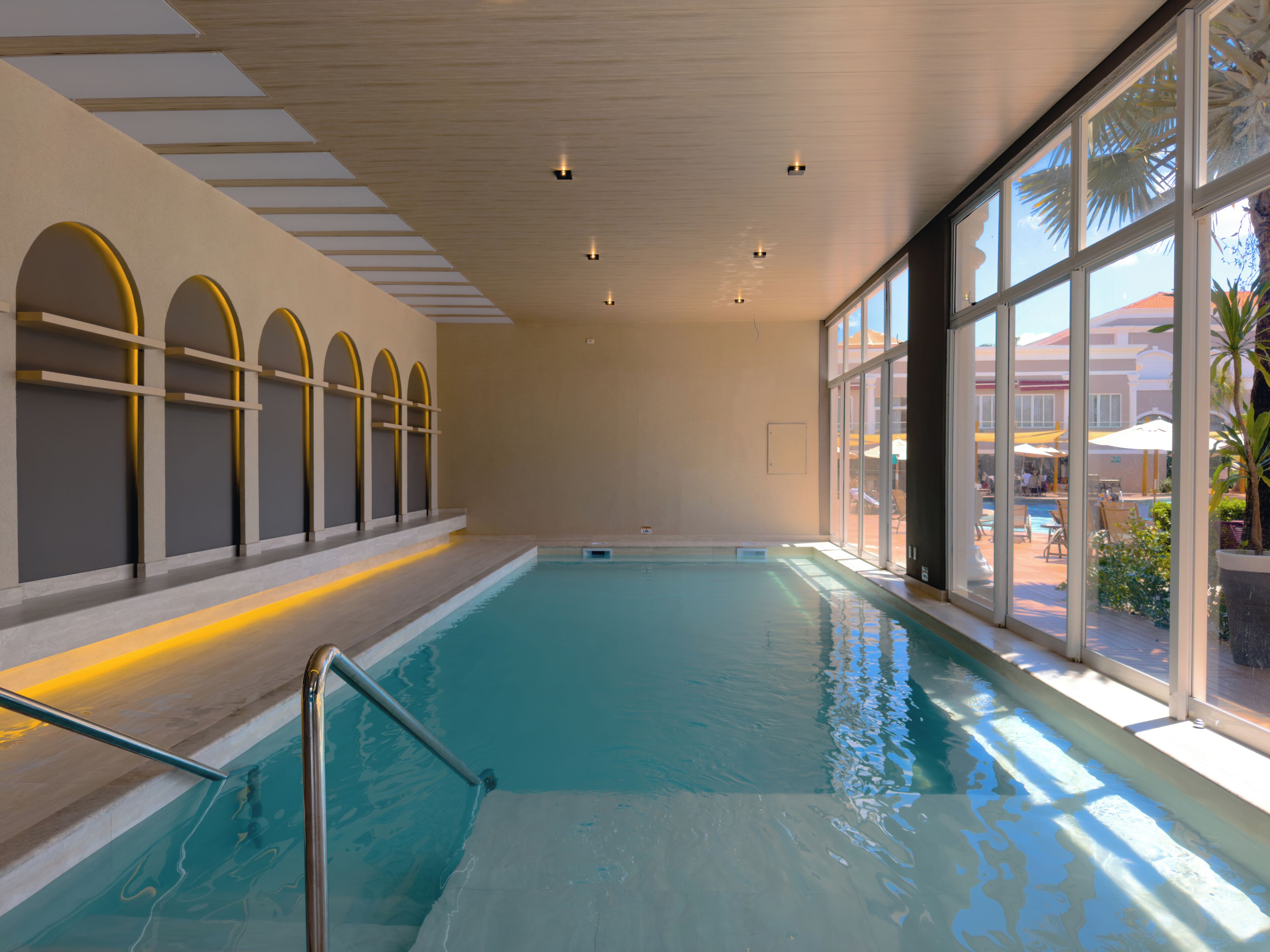 Una piscina interior con paredes de vidrio transparente, suelo de baldosas e iluminación empotrada en el techo.