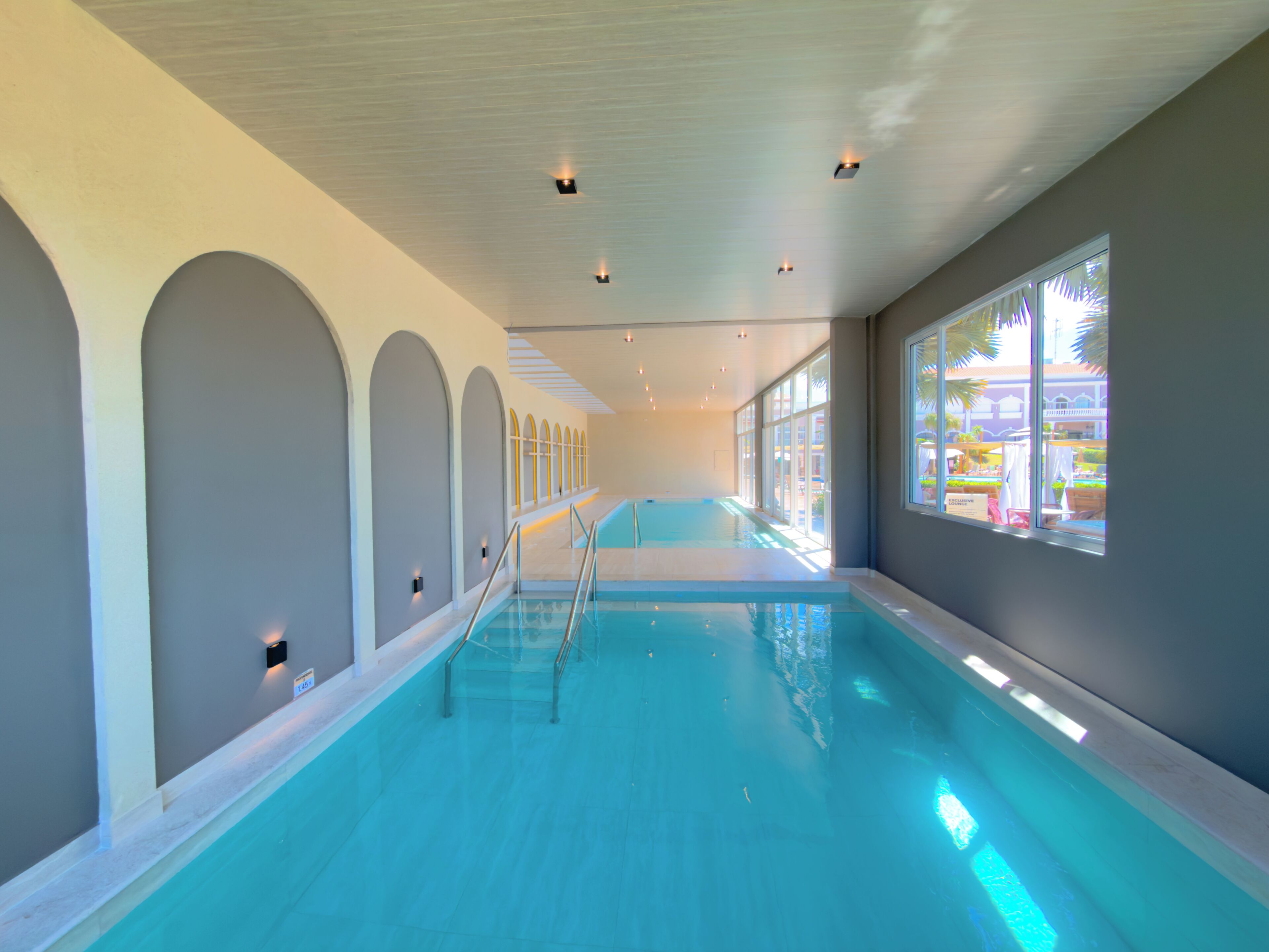 Una piscina interior con agua cristalina, diseños de paredes arqueadas y grandes ventanales que dejan entrar luz natural.