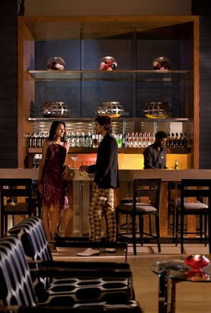 A bar area with a wooden counter, multiple shelves with bottles, and a seating area with patterned chairs. - Courtyard by Marriott Hyderabad (Hyderabad)