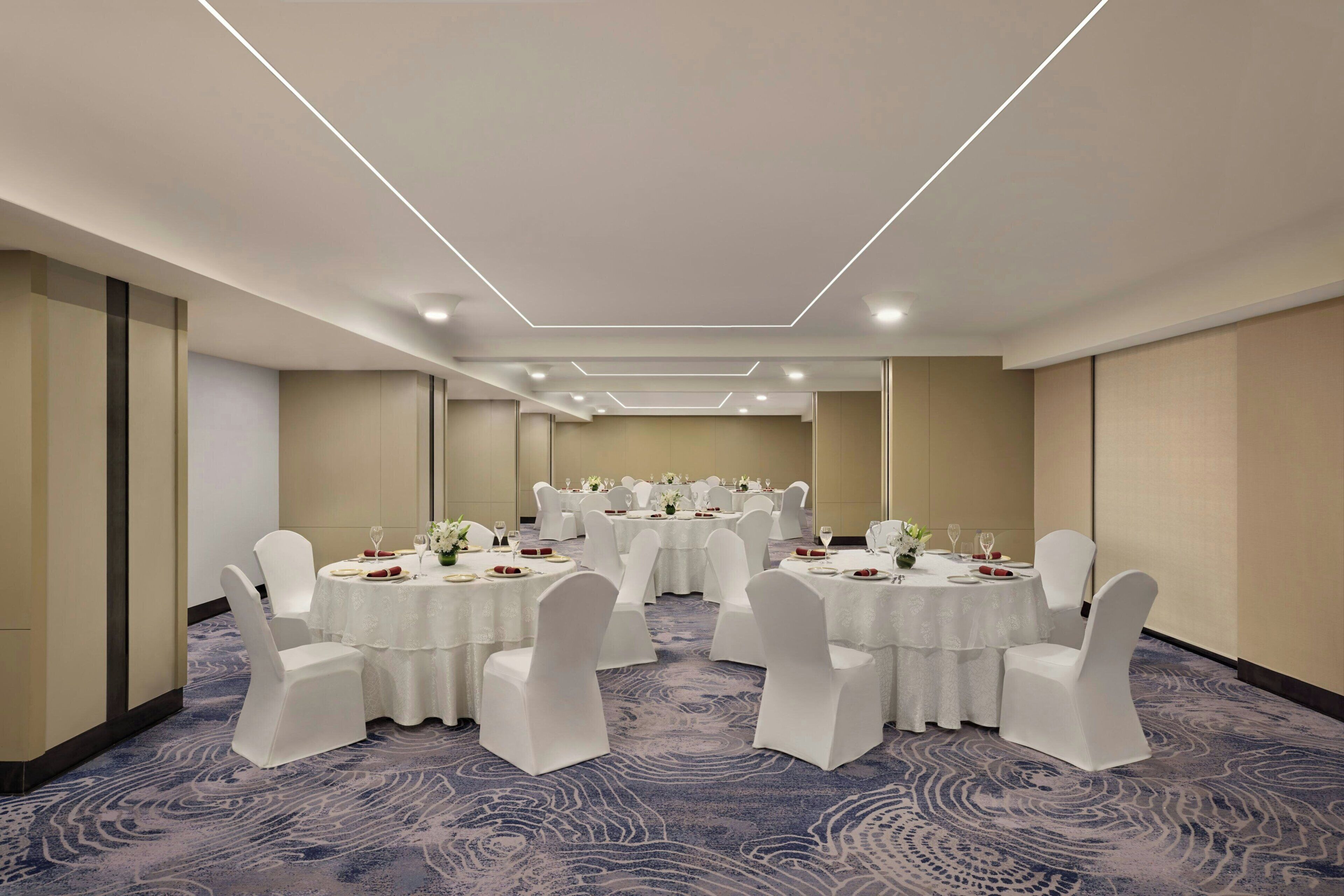 A conference room with round tables, white chairs, and a carpeted floor.
