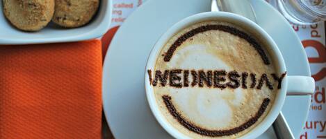 A cup of coffee with a design spelling "WEDNESDAY" on the foam, a spoon, a glass of water, and a plate with cookies.