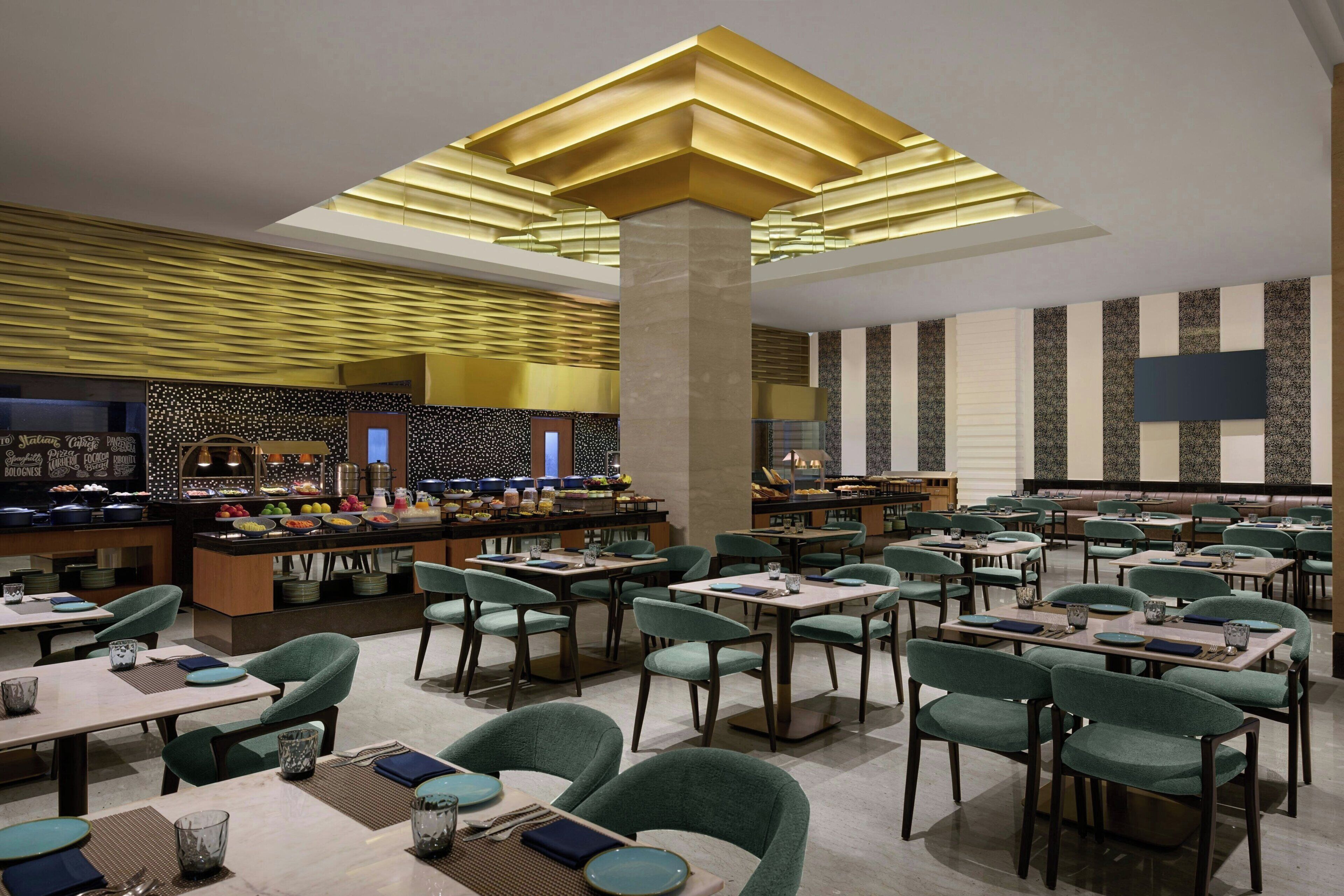 A modern restaurant with a central bar, multiple dining tables, and green upholstered chairs.