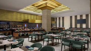 A modern restaurant with a central bar, multiple dining tables, and green upholstered chairs.