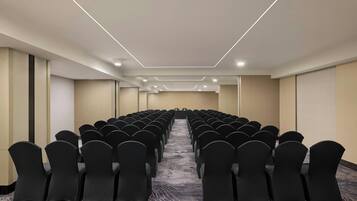Uma sala de conferências com fileiras de cadeiras, piso coberto por carpete e design simples e moderno.