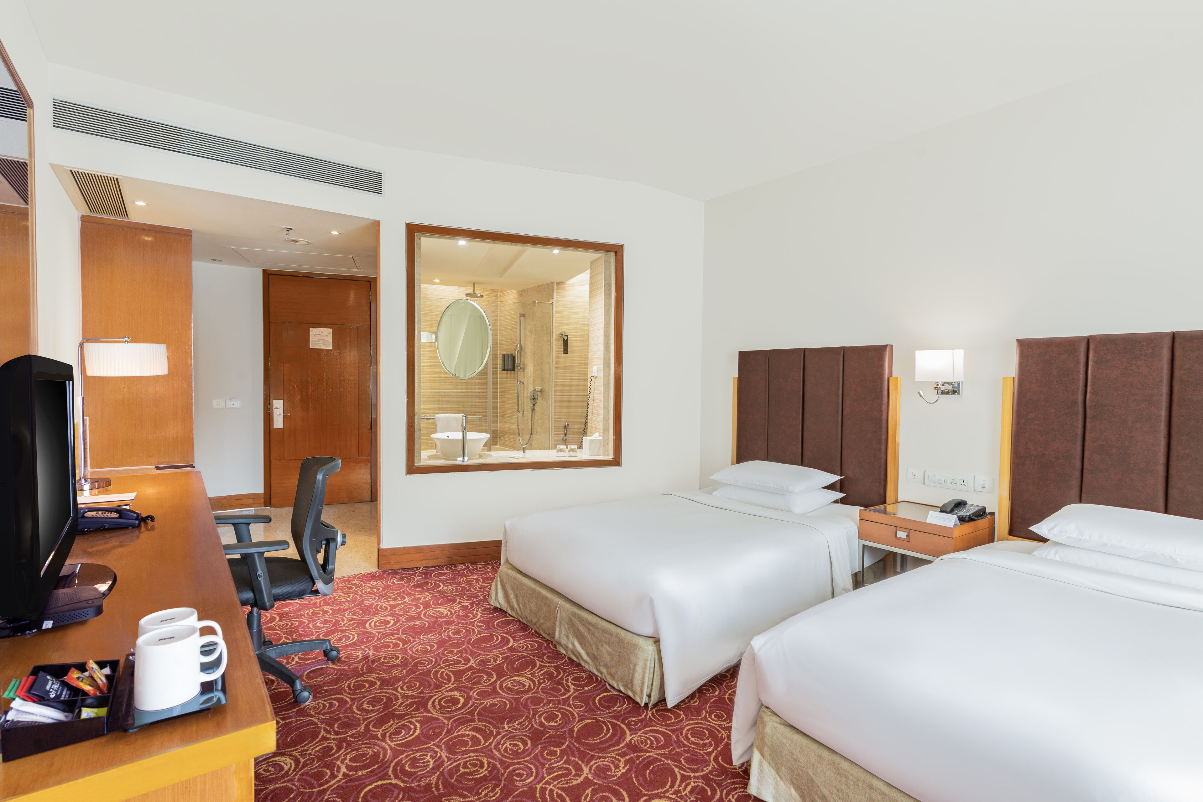 A hotel room with two beds, a desk with a computer and coffee maker, a chair, and a mirror.