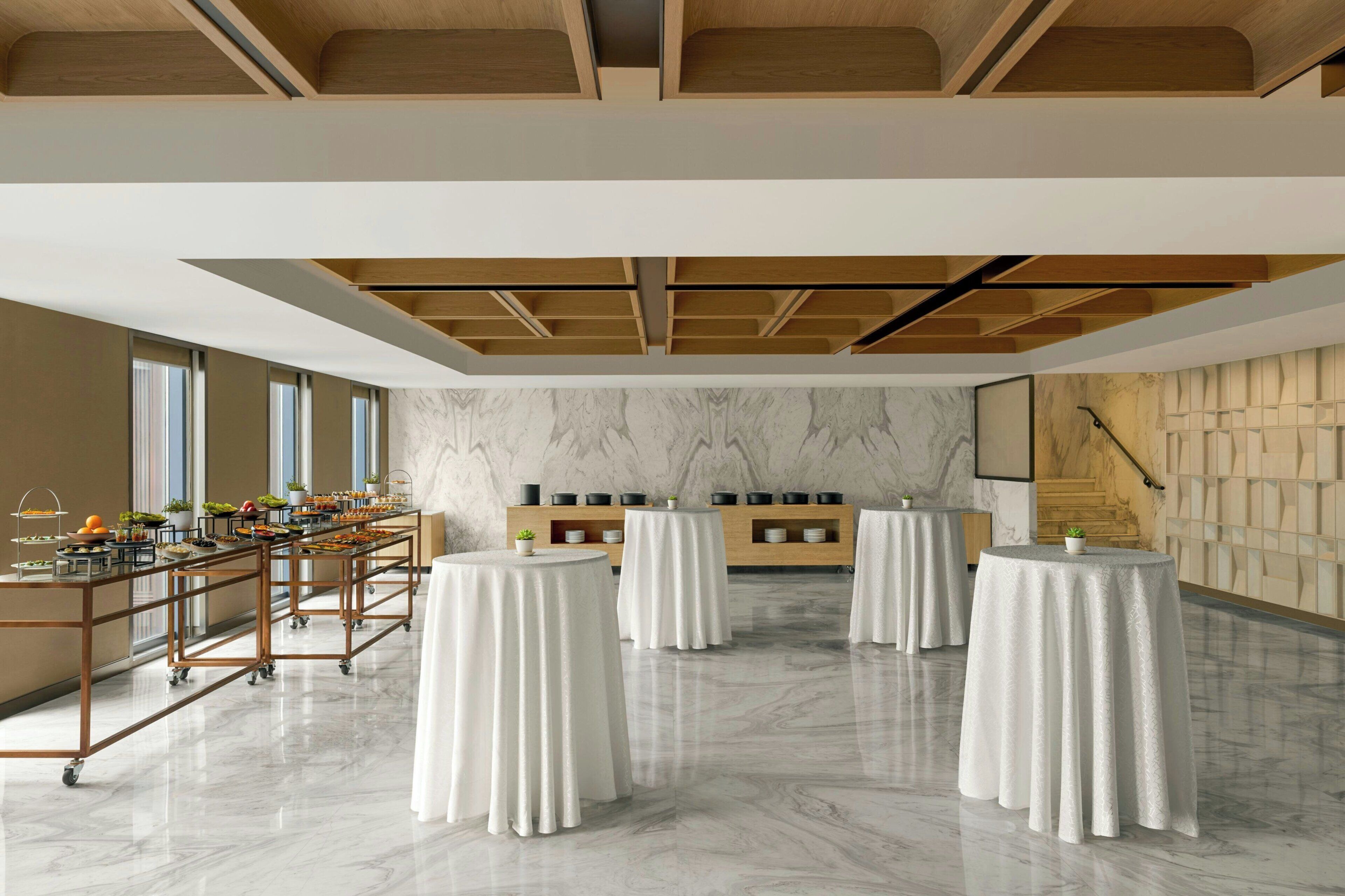 A modern dining area with a marble floor, wooden ceiling beams, and a buffet setup.