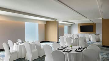 Un salón de conferencias con mesas redondas, sillas blancas y una pantalla grande en la pared.
