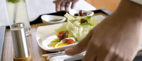 A tray with a salad, a drink, and a salt shaker on a table in a hotel room.