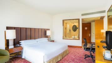 Quarto de hotel com uma cama grande, mesas de cabeceira com luminárias, uma escrivaninha com cadeira, uma televisão e um espelho.