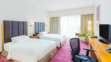 A hotel room with two beds, a desk with a television, a chair, and a window with curtains.