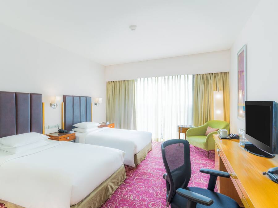 A hotel room with two beds, a desk with a television, a chair, and a window with curtains.