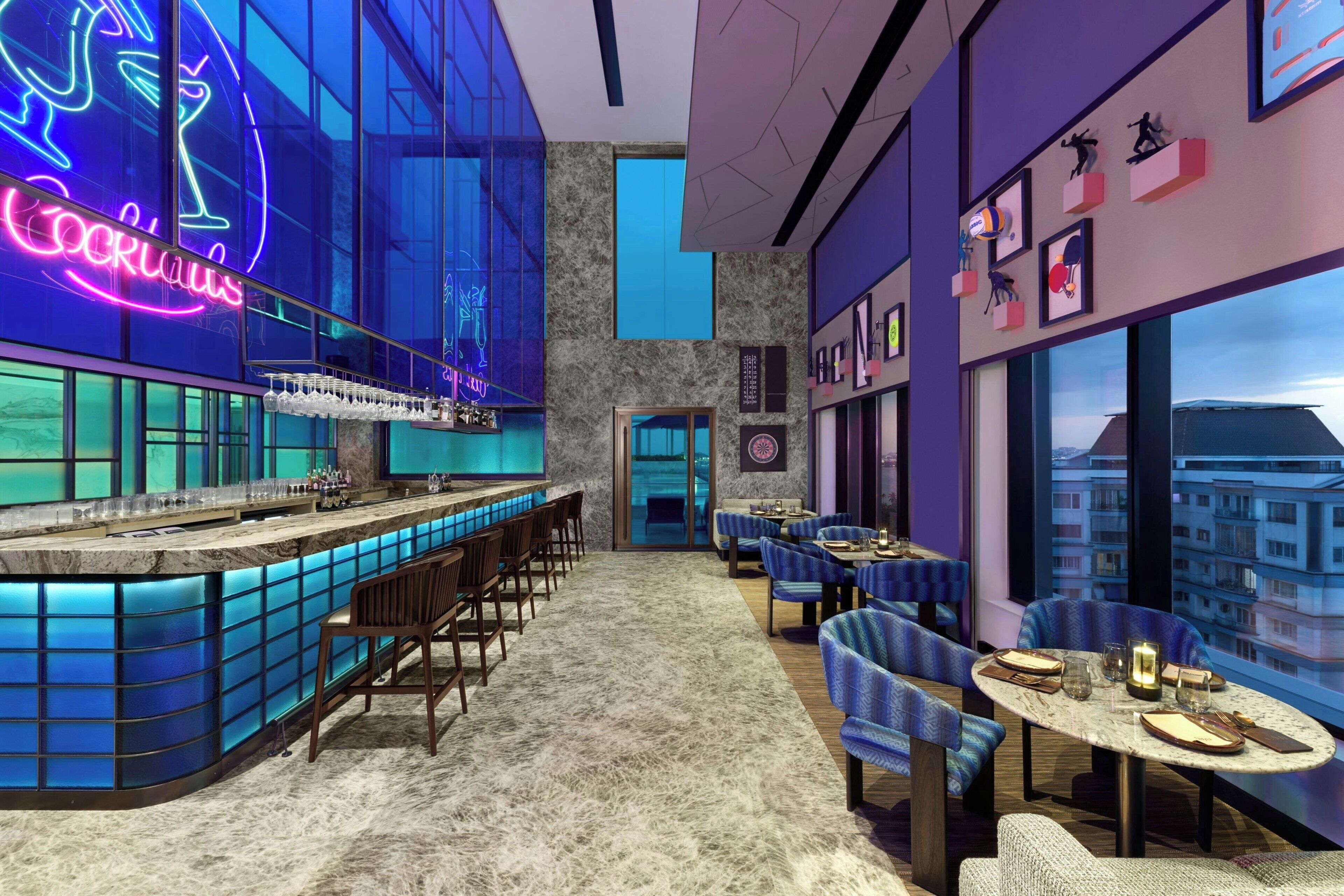 A modern bar area with a neon sign, seating arrangements, and a view of the cityscape.