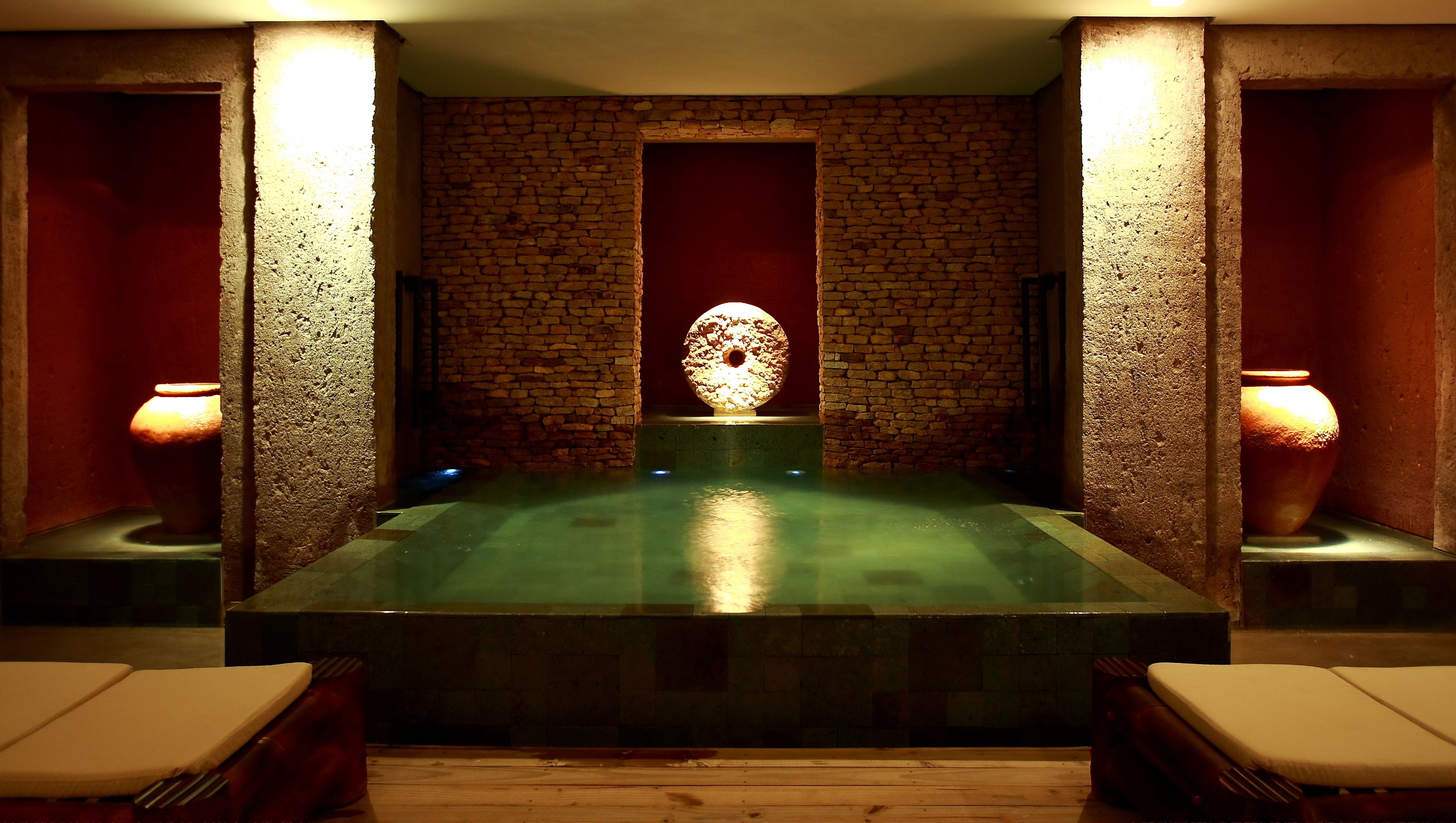 A spa room with a stone wall, a central water feature, and two side lamps.