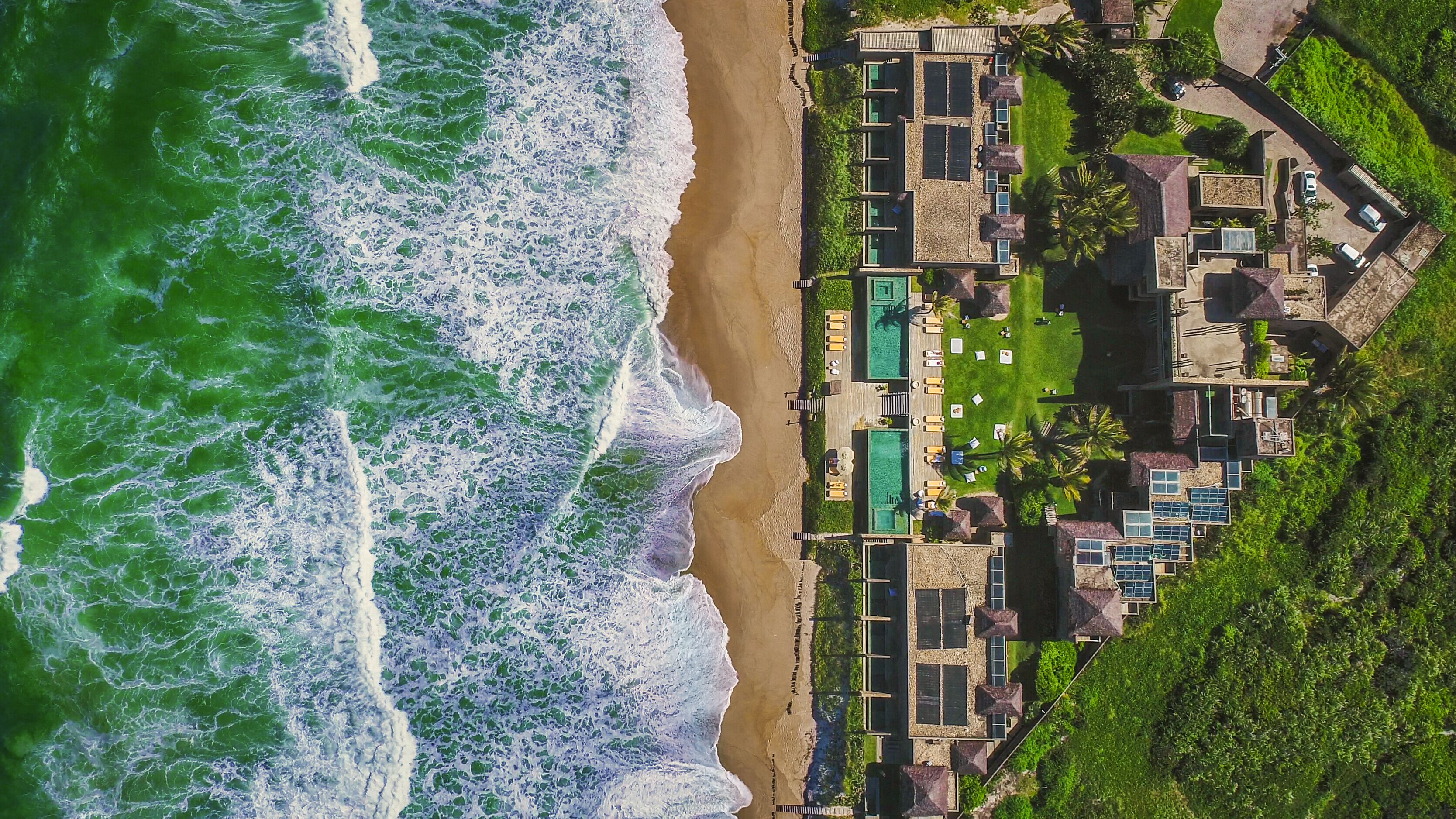 An aerial view of a coastal hotel with multiple buildings, a beach, and a well-maintained lawn.