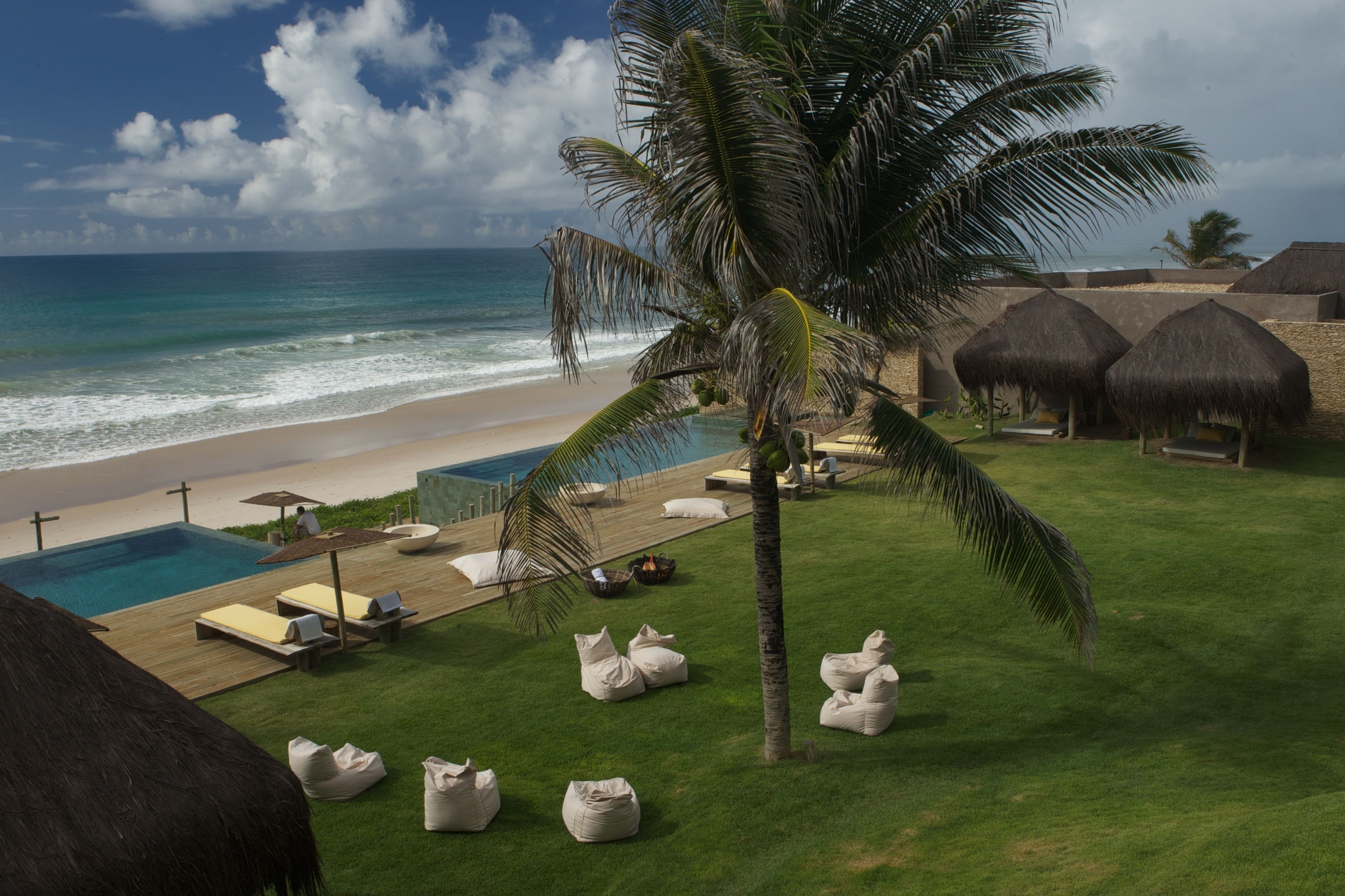 Um resort à beira-mar com piscina, espreguiçadeiras e cabanas com telhado de palha.