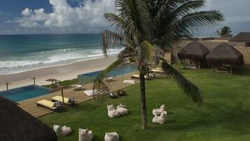 Um resort à beira-mar com piscina, espreguiçadeiras e cabanas com telhado de palha.