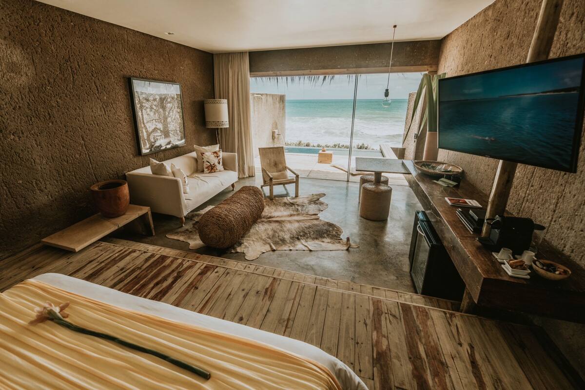 A bedroom with a large bed, a sofa, a TV, a desk with a computer, and a view of the ocean.