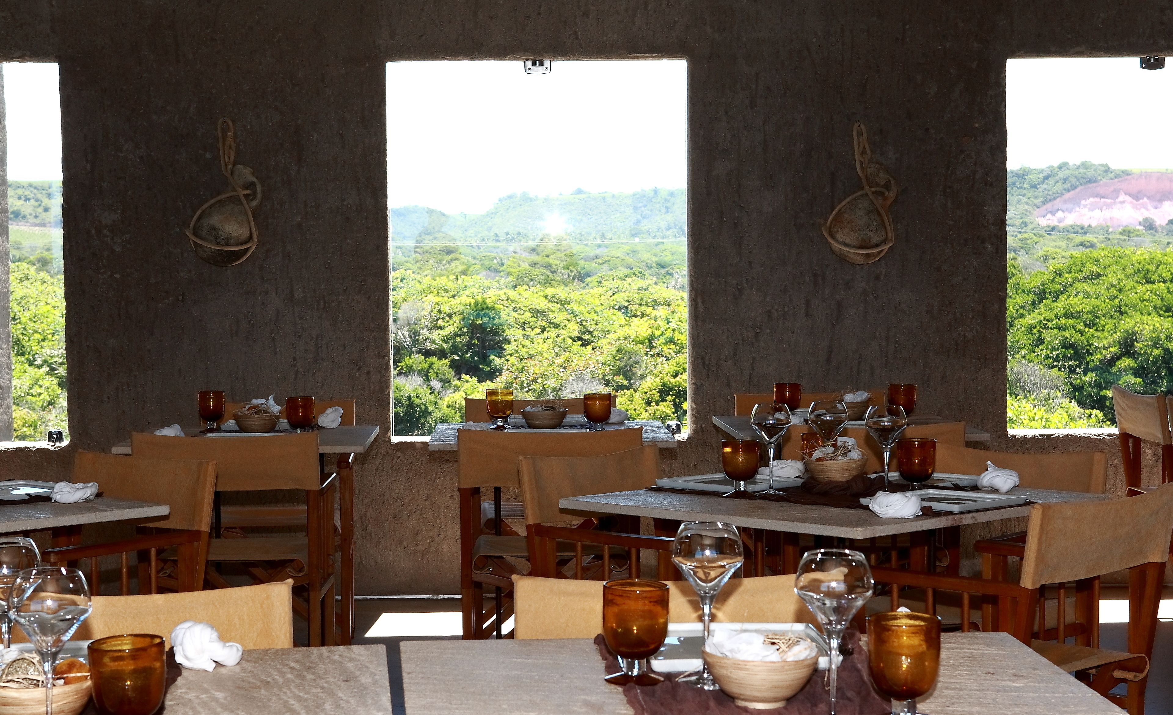 Un restaurante con mesas dispuestas para comer, cada una con copas de vino y cuencos, con vistas a un exuberante paisaje verde.