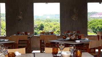 Un restaurante con mesas dispuestas para comer, cada una con copas de vino y cuencos, con vistas a un exuberante paisaje verde.