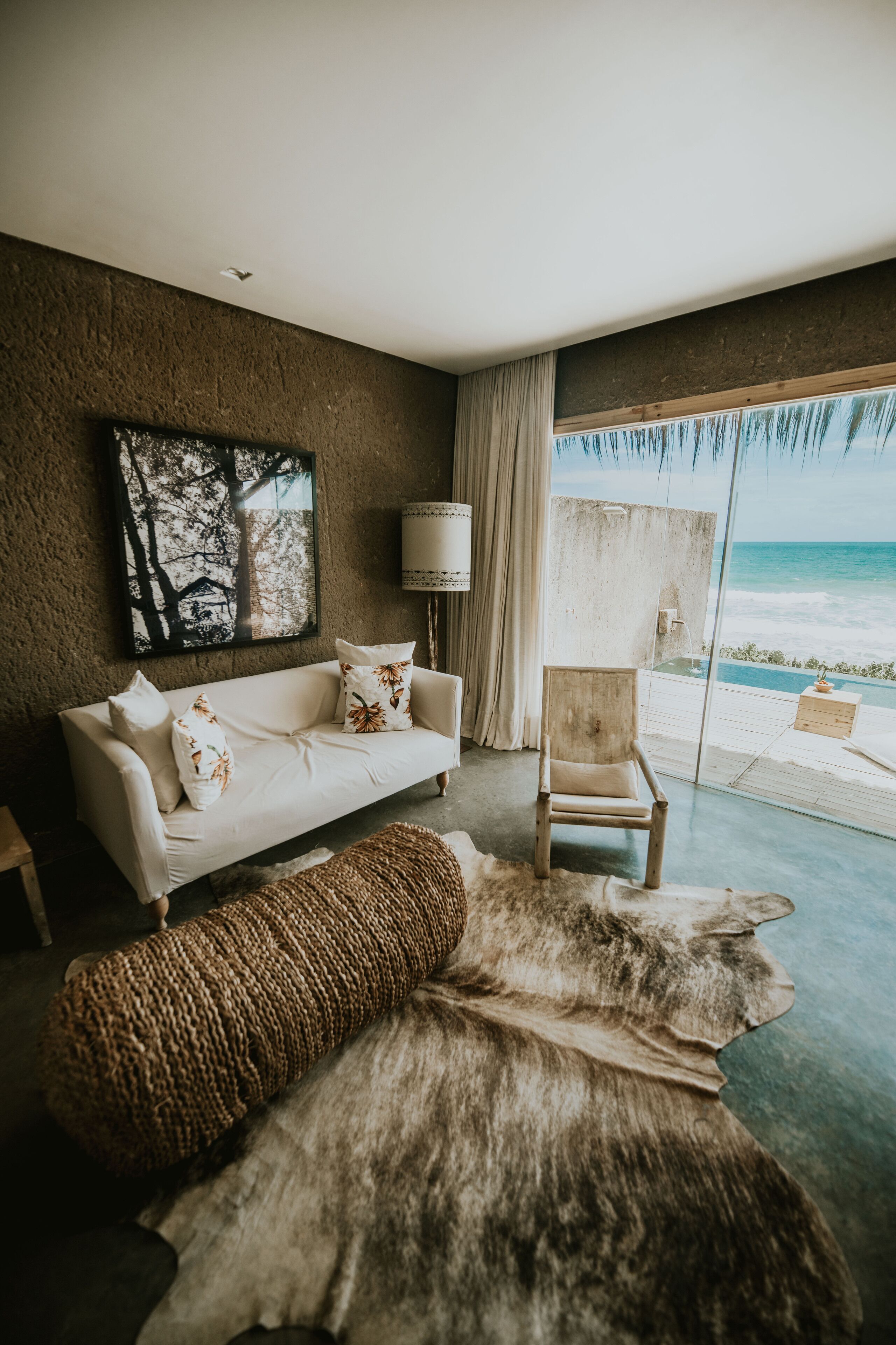 A room with a white sofa, a wooden chair, a large rug, and a painting of trees.