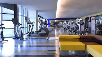 A gym with exercise equipment, a yellow couch, and large windows.