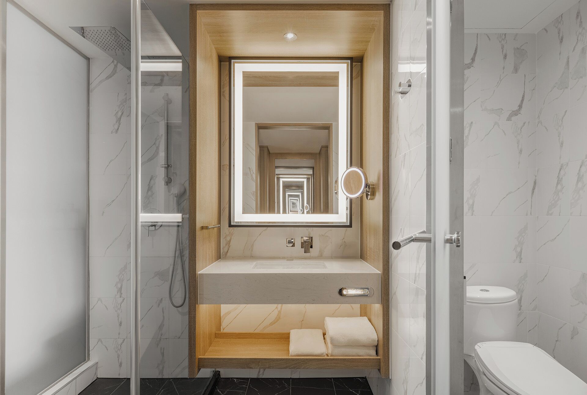 A modern bathroom with a glass-enclosed shower, a wooden vanity, and a toilet.