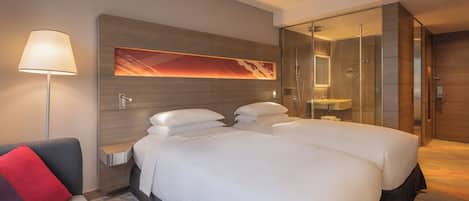 Ein Hotelzimmer mit zwei Betten, einem Nachttisch, einer Lampe, einem großen abstrakten Kunstwerk, einer Duschkabine aus Glas und einem Kleiderschrank.
