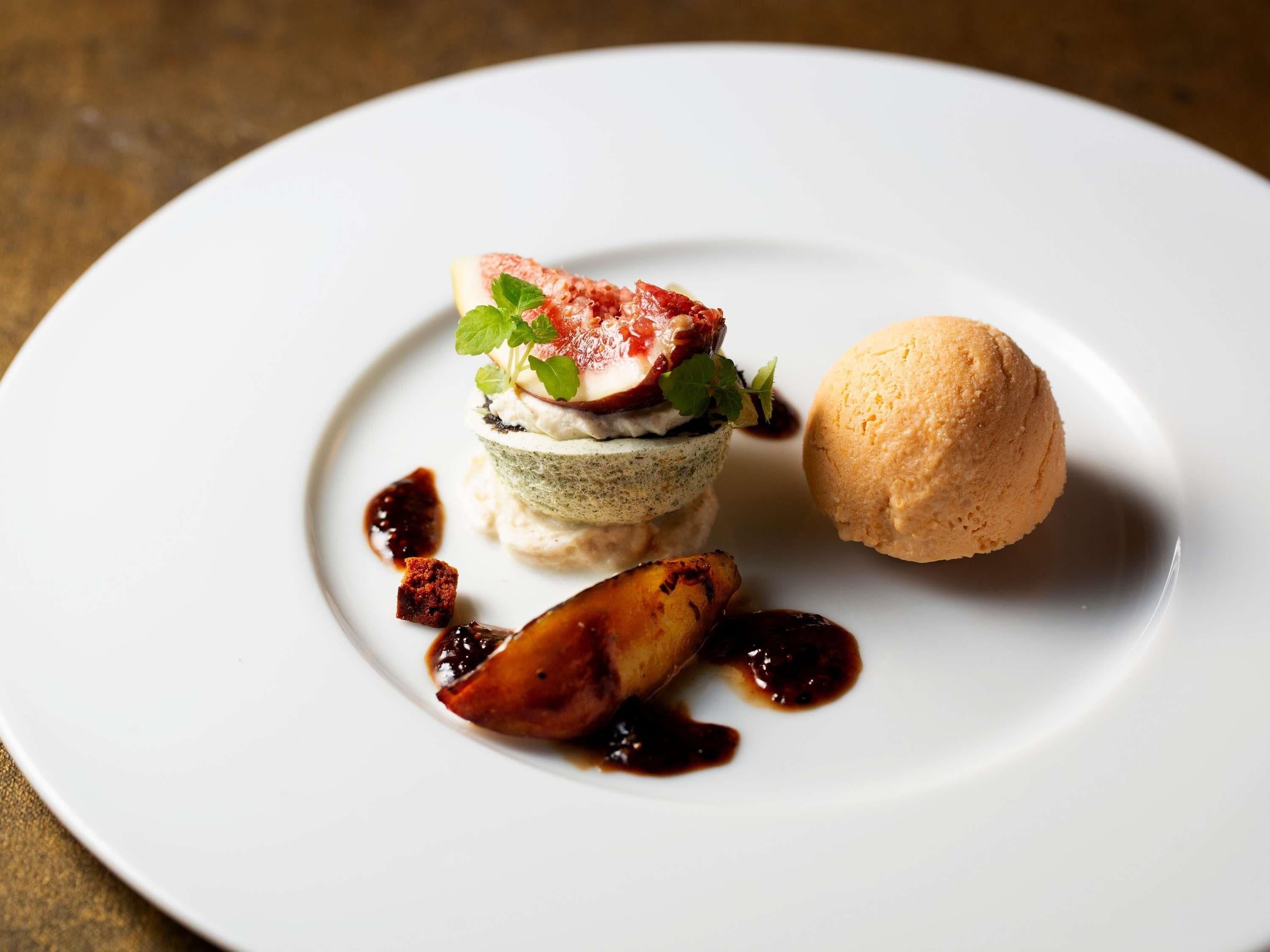 A dessert plate with a layered cake, a scoop of ice cream, and grilled fruit.