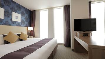 A hotel room with a large bed, a flat-screen TV, a desk, and a window with curtains.