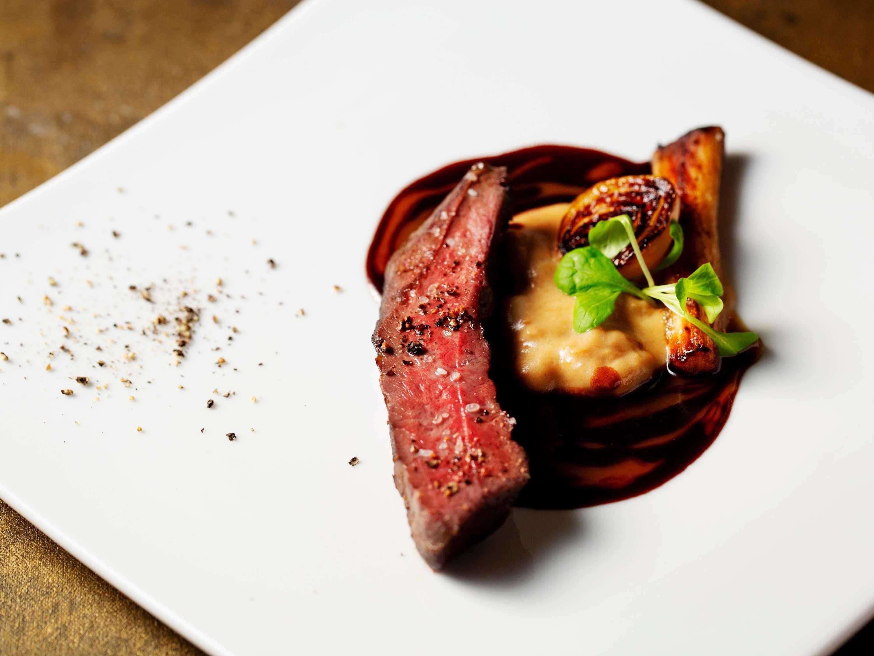 Une assiette blanche avec un steak, une sauce et quelques légumes verts.