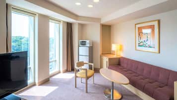 Ein Hotelzimmer mit Fernseher, einer Couch, einem Esstisch, einem Stuhl, einer Lampe, einer Mikrowelle und einem Gemälde.