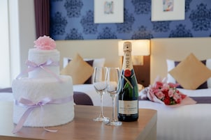 Un pastel de bodas de tres niveles con una flor rosa en la parte superior, dos copas de champán y una botella de Moët & Chandon sobre una mesa de madera en una habitación de hotel.