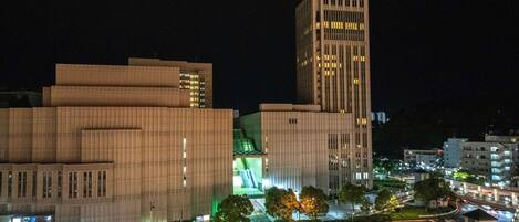 A nighttime cityscape with modern buildings, a prominent tower, and a well-lit intersection.