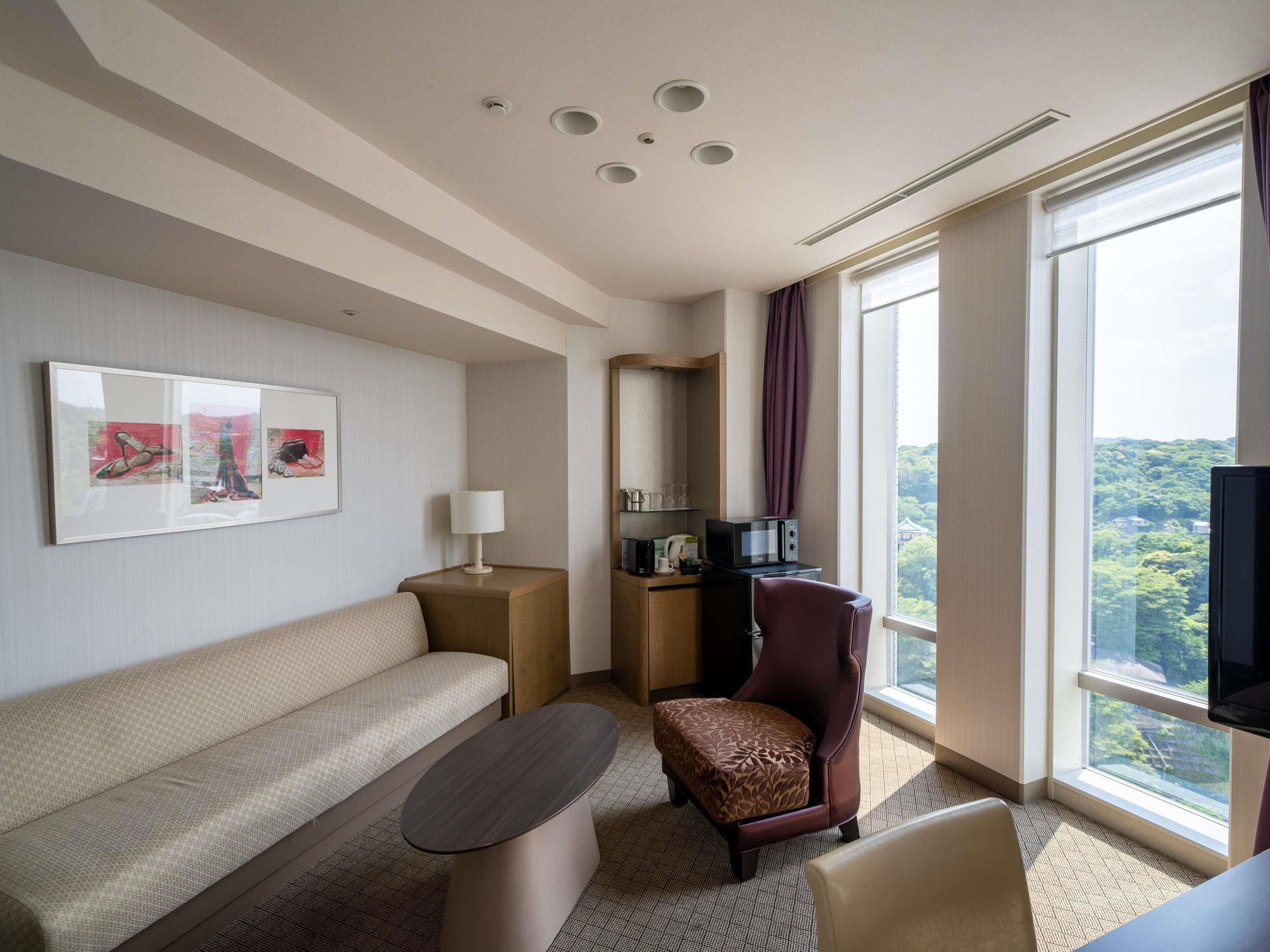 A hotel room with a sofa, armchair, small table, and a TV.