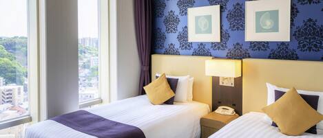 A hotel room with two beds, a city view, patterned wallpaper, and framed artwork on the wall.