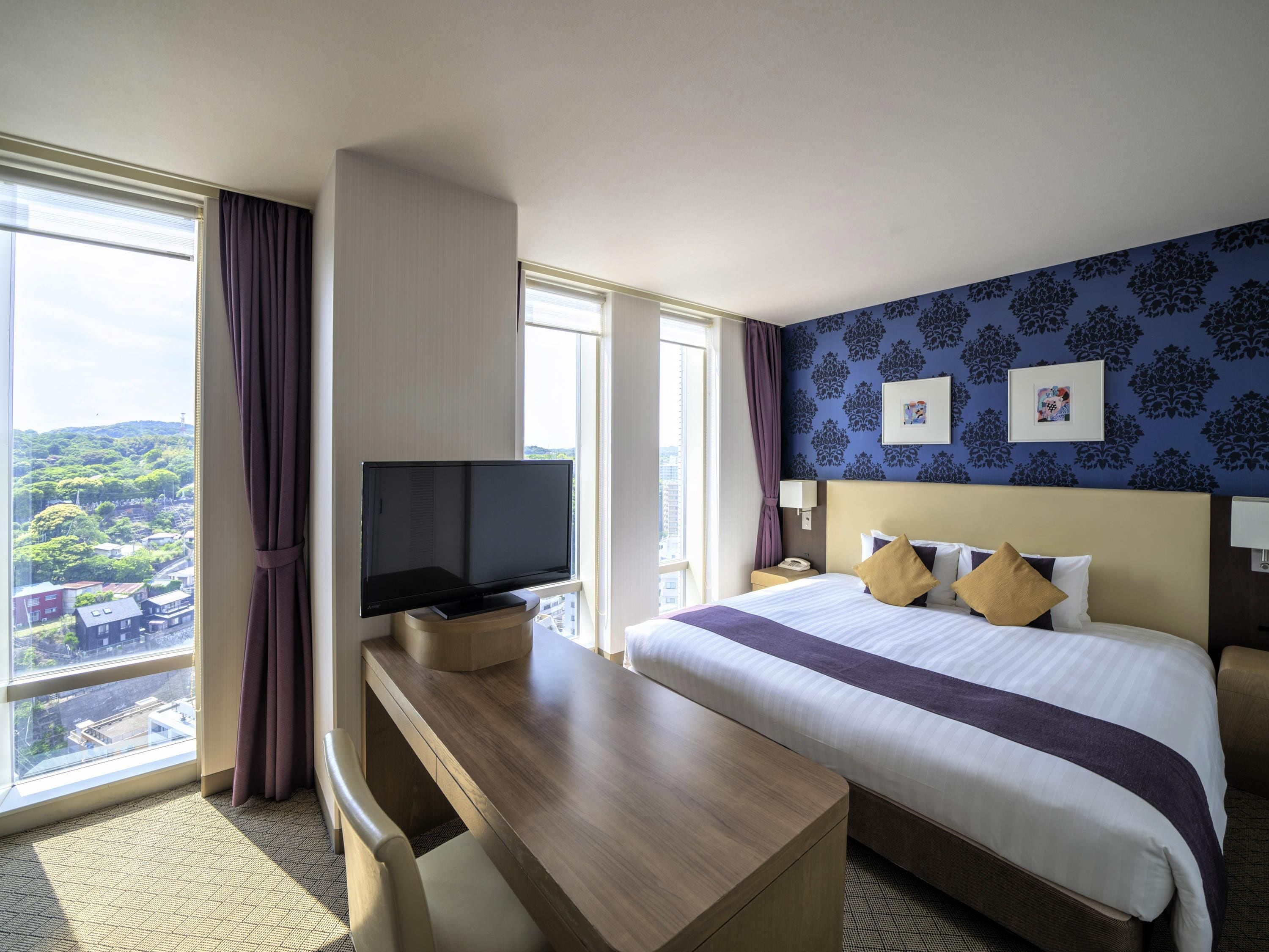 Een hotelkamer met een bed, een bureau, een televisie, een nachtkastje en een raam met gordijnen.