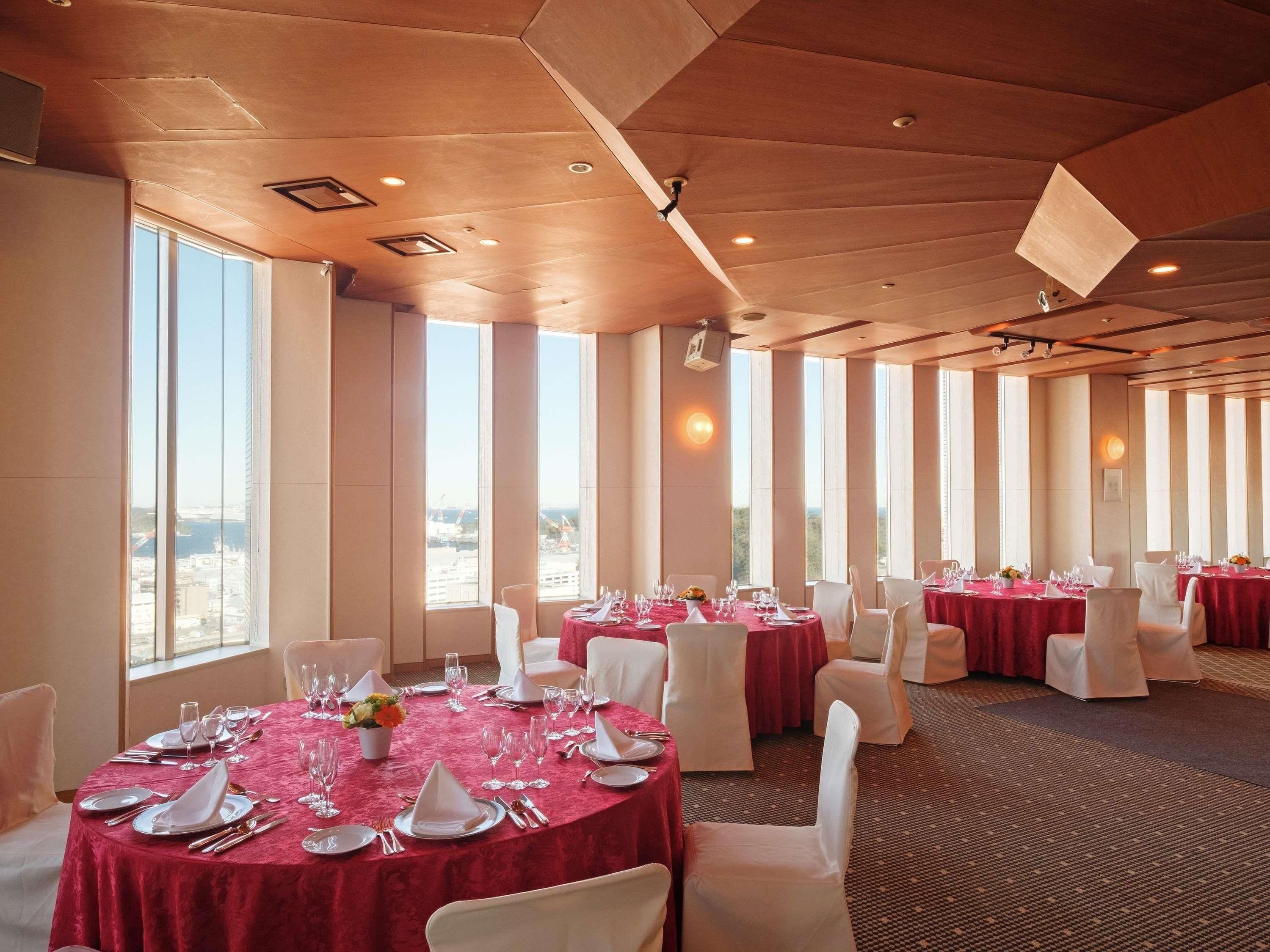 Un salón de banquetes con mesas redondas, sillas blancas y manteles rojos.