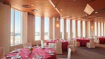 Un salón de banquetes con mesas redondas, sillas blancas y manteles rojos.