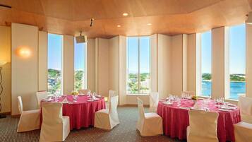 A dining area with tables set for four, large windows with a view of the sea, and a patterned carpet.