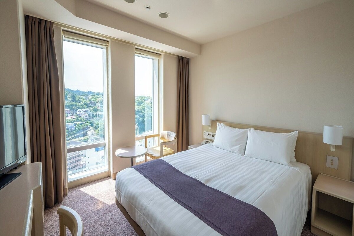 A hotel room with a large bed, a desk, a chair, and a TV.