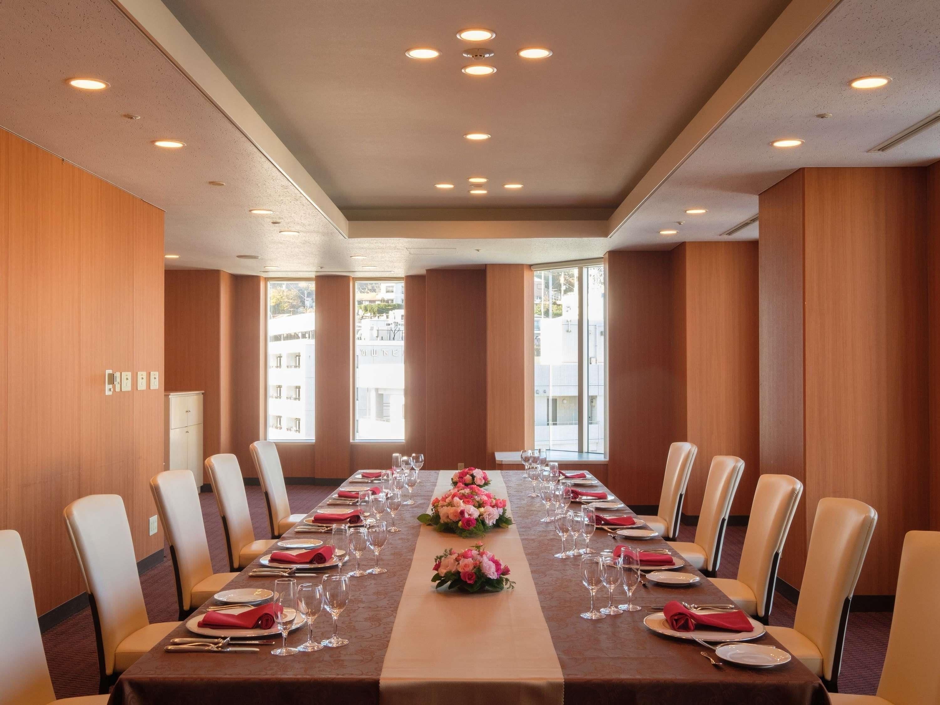 A conference room with a long table set for a meeting, equipped with chairs, tables, and a decorative centerpiece.