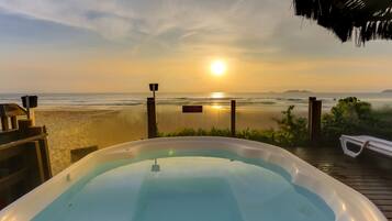 A hot tub on a wooden deck overlooking a beach with a sunset in the background.