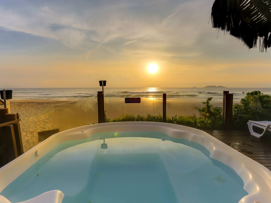 A hot tub on a wooden deck overlooking a beach with a sunset in the background.
