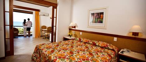 A hotel room with a bed, a nightstand with a phone, a picture on the wall, and a view of the outside balcony.