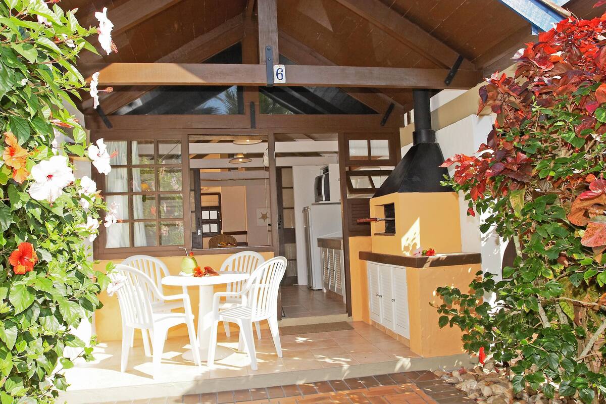 A covered outdoor dining area with white chairs and a table, a kitchen area with a stove, and a number 6 sign above the entrance.